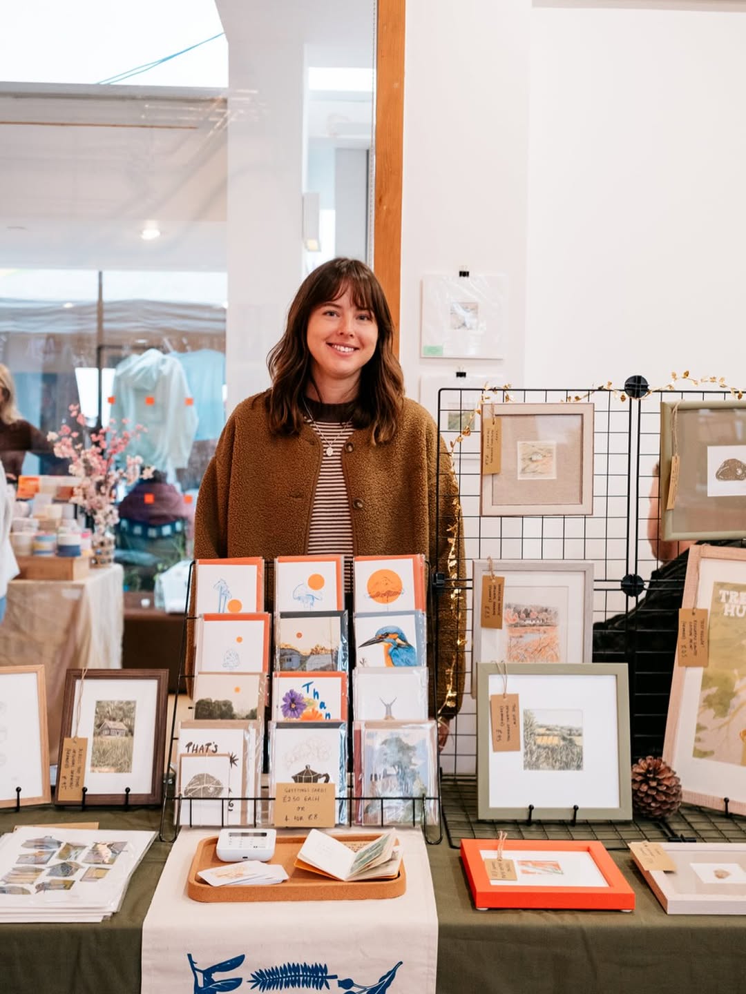Emma Britten artist stands behind a display of art prints